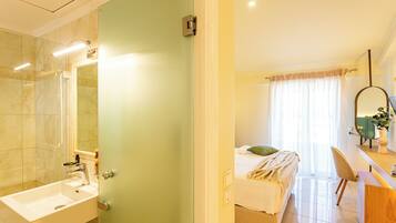 A hotel room with a bathroom, a bed, a desk, and a mirror.