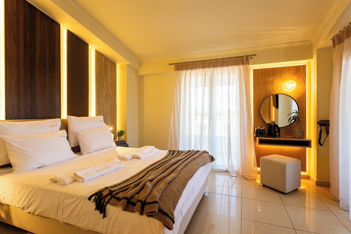A hotel room with a large bed, a bedside table with a lamp, a mirror, and a small seating area.