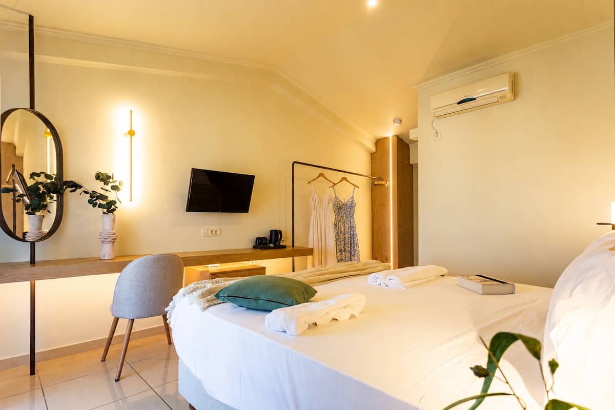 A hotel room with a bed, a desk, a chair, a TV, a mirror, and a wardrobe.