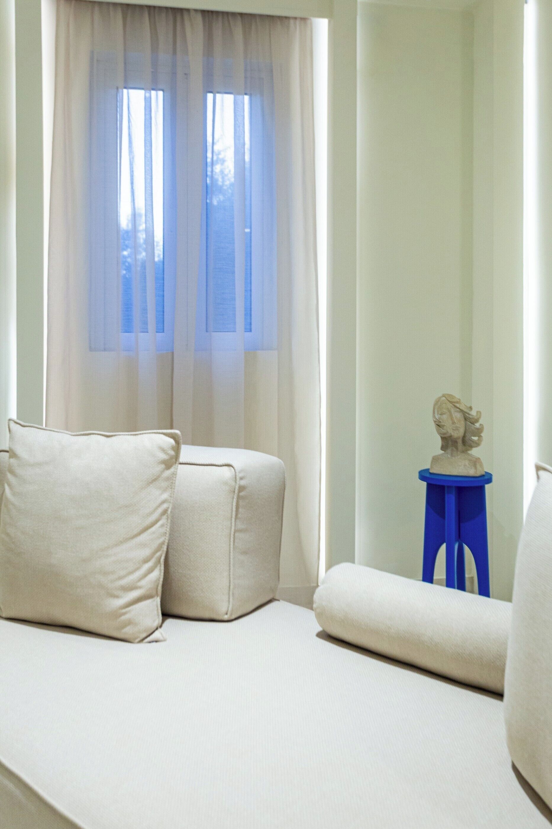 Habitació amb sofà, una taula petita i una escultura de bust, i cortines translúcides.