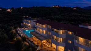A multi-story hotel with a swimming pool, outdoor seating, and a view of the surrounding landscape. - Zante Pantheon Hotel (Zakynthos)