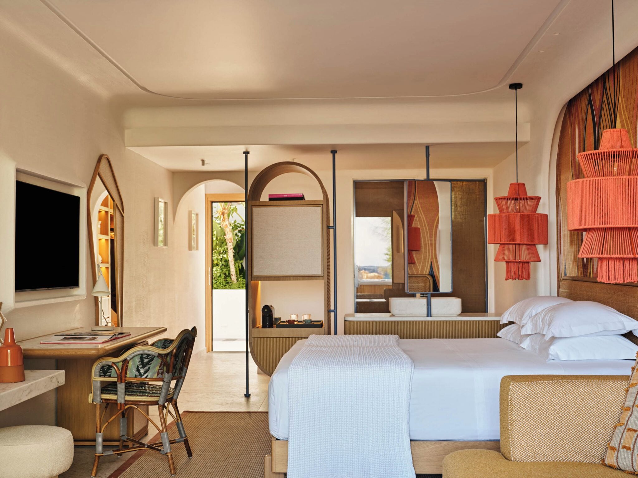 A hotel room with a bed, a desk, a chair, a television, and a bathroom with a mirror and sink.