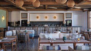 A restaurant with wicker furniture, a bar area, and a patterned floor. - Myconian Sunrise Relais & Chateaux Hotel (Mykonos)