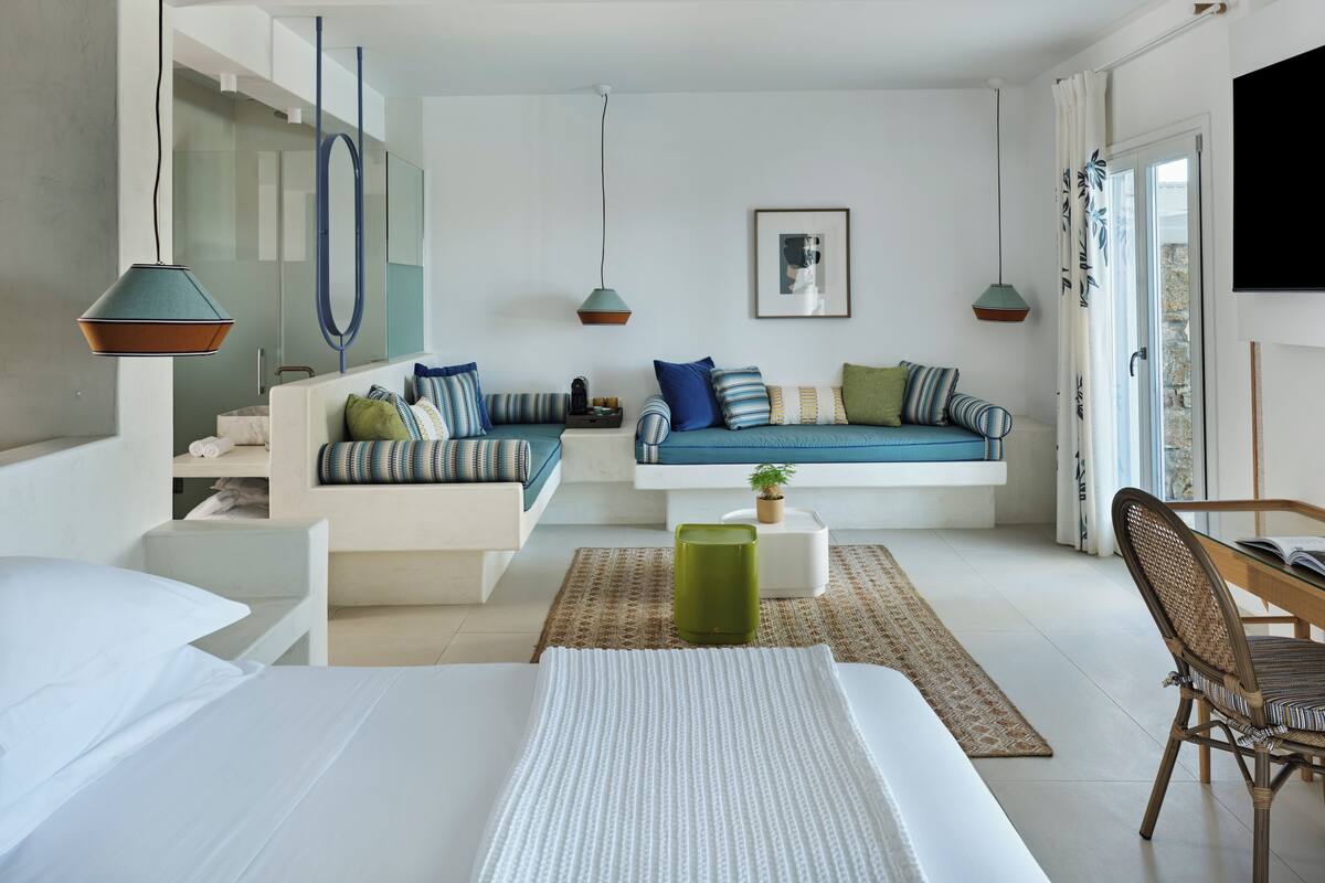 A modern living room with a sofa, a coffee table, and a chair. There is a television mounted on the wall and a window with curtains.