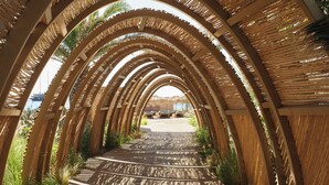 A wooden pathway with a series of arches leading to a distant view. - Myconian Sunrise Relais & Chateaux Hotel (Mykonos)