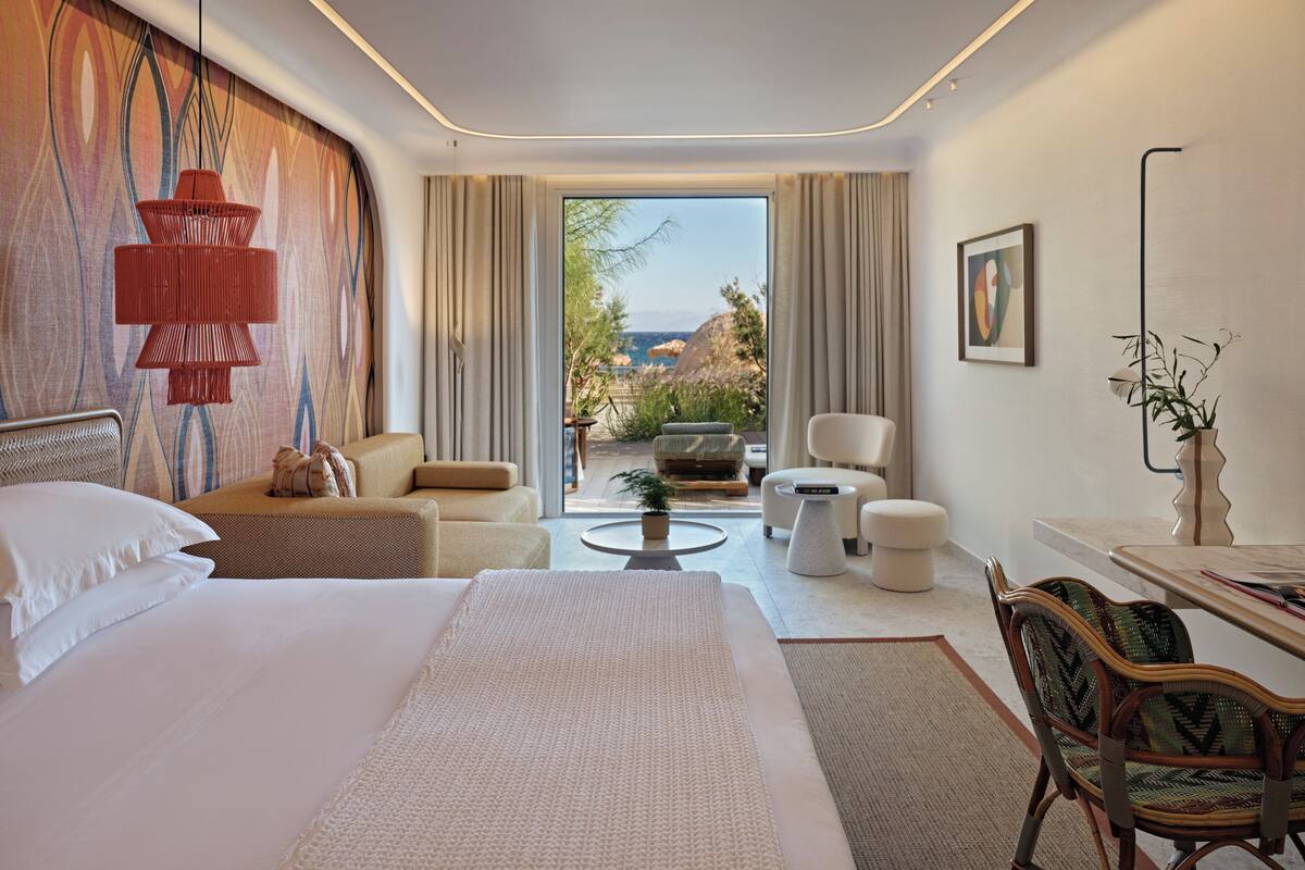 A modern hotel room with a large bed, a sitting area with a view, and a dining area.