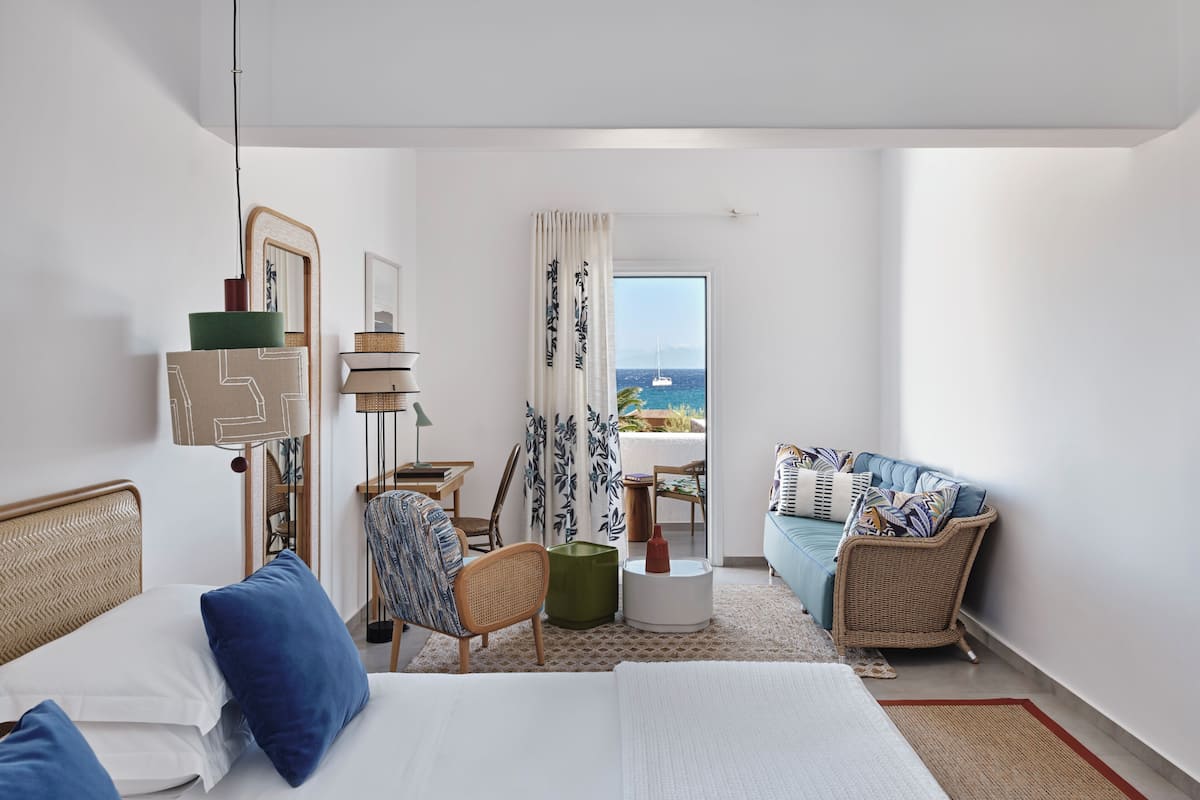 A hotel room with a bed, a sofa, a chair, a small table, and a view of the sea.