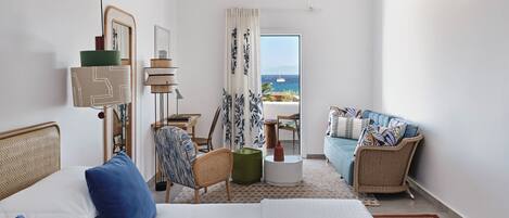 A hotel room with a bed, a sofa, a chair, a small table, and a view of the sea.