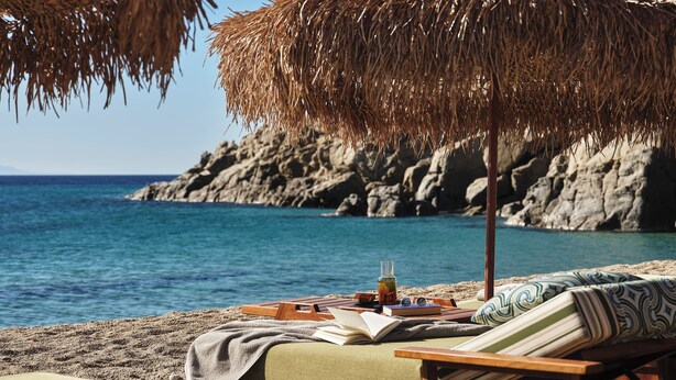 A beachside lounge with a view of the sea and rocky cliffs. - Myconian Sunrise Relais & Chateaux Hotel (Mykonos)