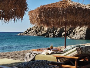 A beachside lounge with a view of the sea and rocky cliffs. - Myconian Sunrise Relais & Chateaux Hotel (Mykonos)