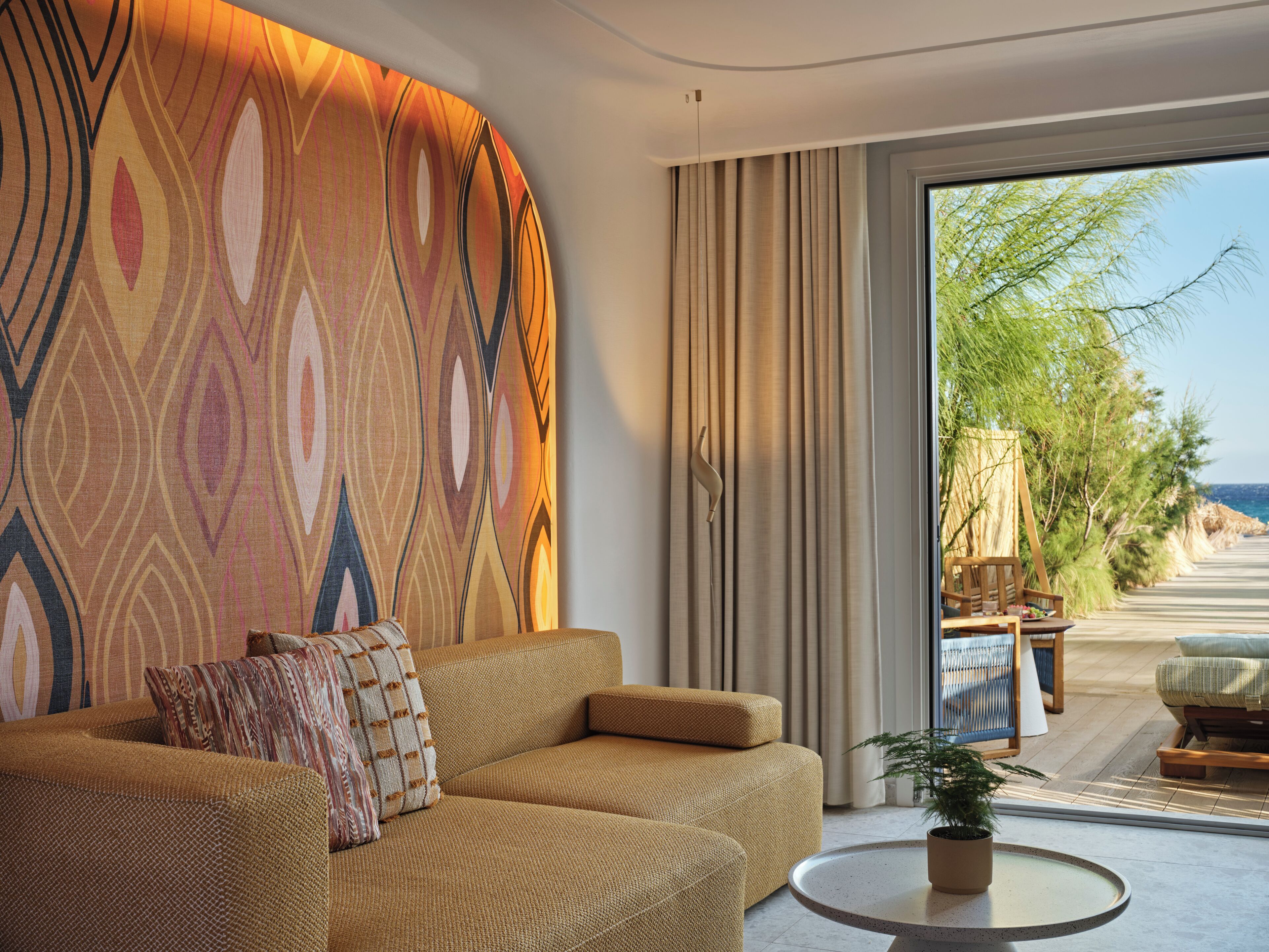 Una sala de estar moderna con pared decorada, un sofá, una mesa de centro y vistas a una playa y palmeras.