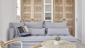 A modern living room with a grey sofa, a round wooden coffee table, and a wicker chair. - Boho Suites (Mykonos)