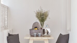 A cozy corner with two white cushioned chairs, a small wooden table with a basket and a vase of flowers, and a woven mat on the floor. - Boho Suites (Mykonos)