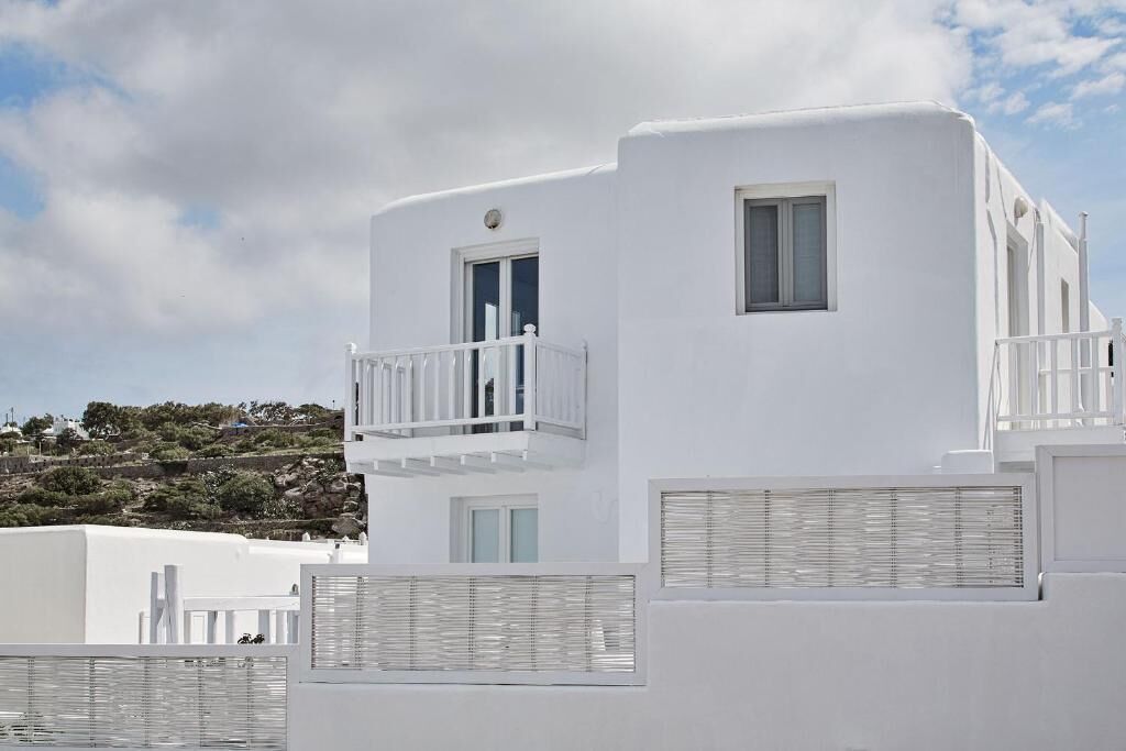 A white building with balconies, windows, and a view of a hillside.