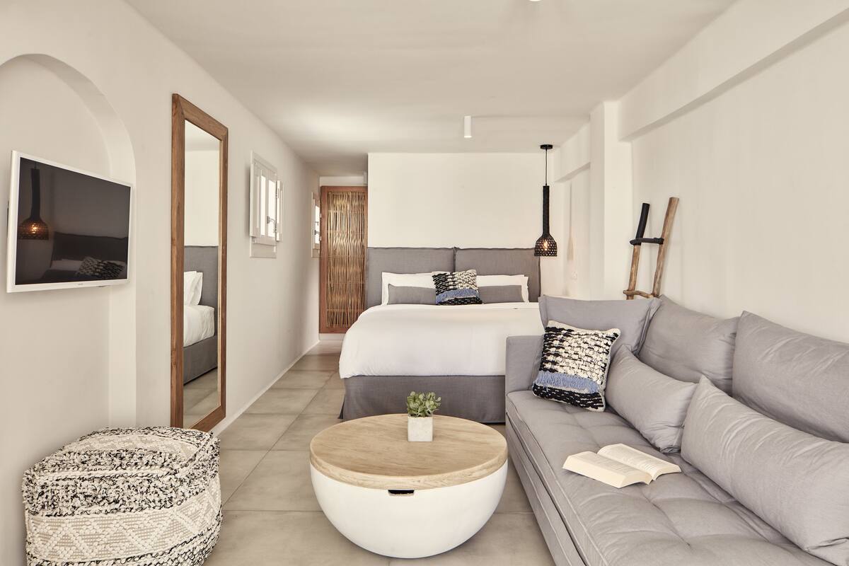 A modern bedroom with a bed, a grey sofa, a round coffee table, and a small round ottoman.