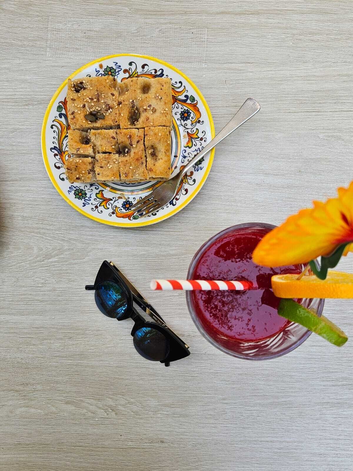 A plate of food, a drink with a straw, and a pair of sunglasses on a wooden surface.