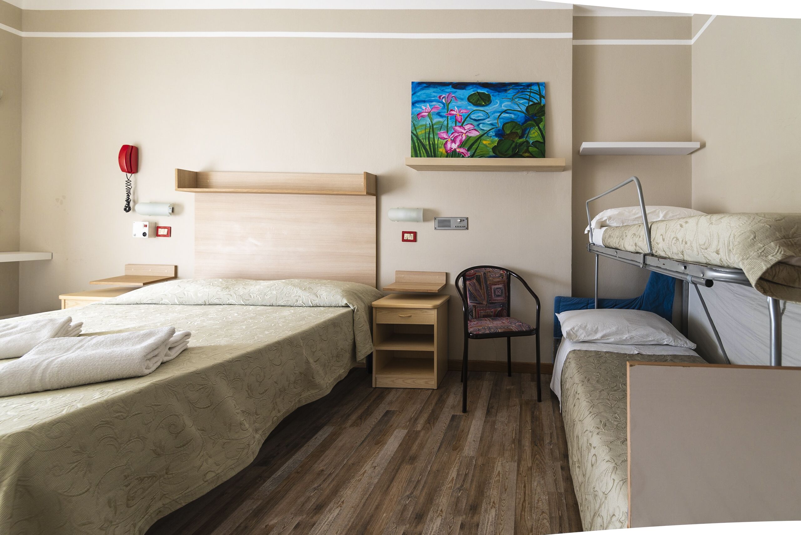 Een hotelkamer met twee eenpersoonsbedden, een bureau, een stoel, een stapelbed en een schilderij aan de muur.