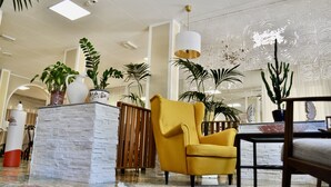Un hall d’entrée spacieux, avec un fauteuil jaune, un bac à fleurs en pierre blanche et diverses plantes en pot.