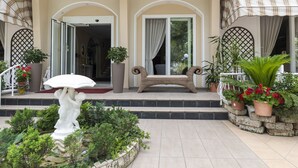 L’entrée d’un hôtel, avec une statue tenant un parapluie, un banc en osier et des plantes en pot.