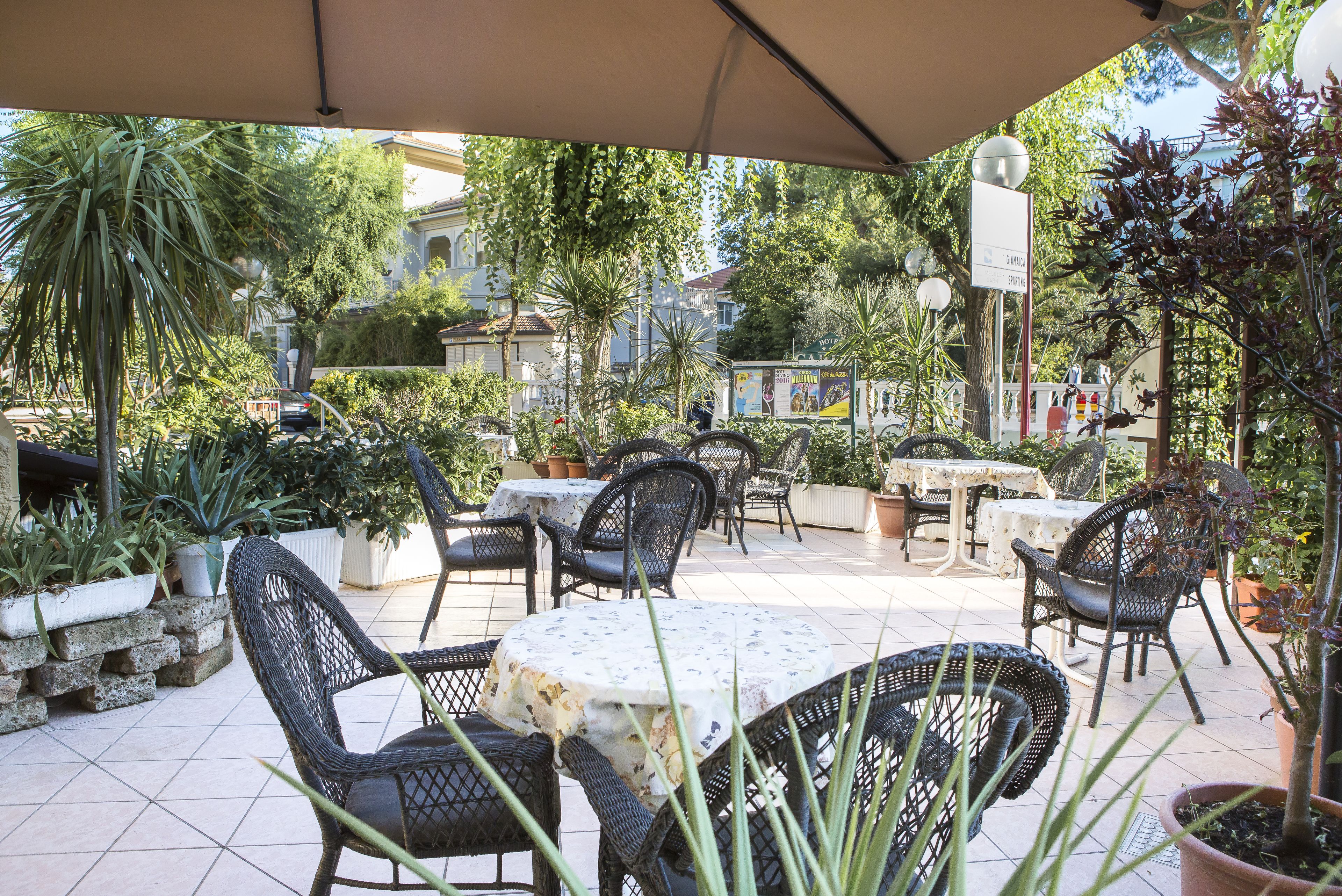 An outdoor patio with wicker furniture, potted plants, and a tiled floor.