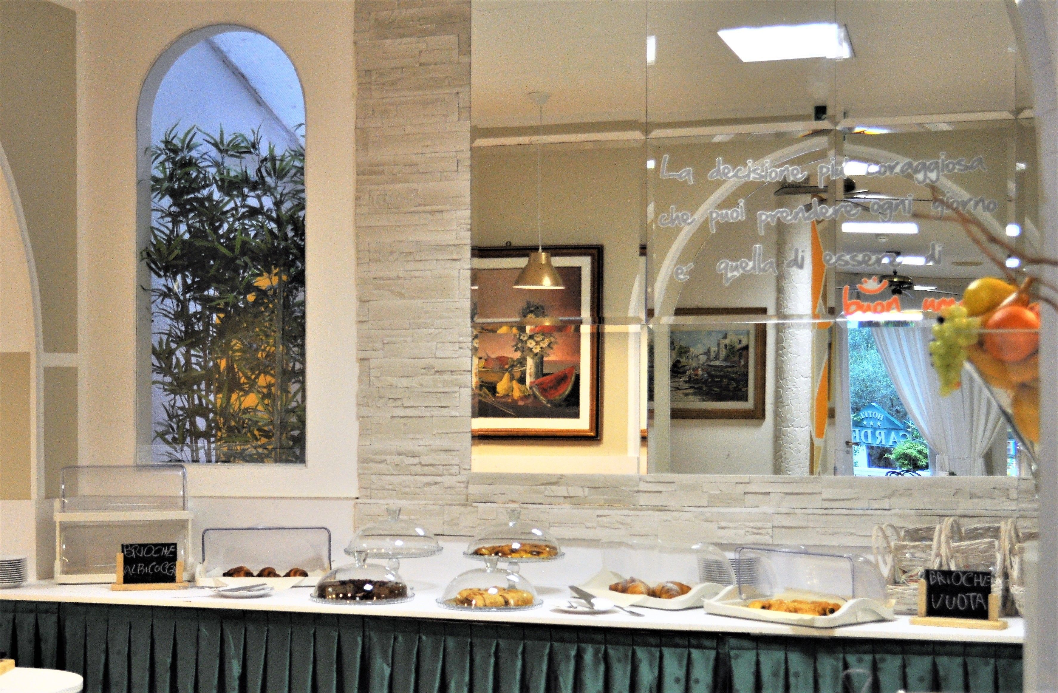 Buffet de l'esmorzar amb diversos aliments exposats en recipients transparents, un quadre de pissarra i un mirall decoratiu que reflecteix l'interior de la sala.
