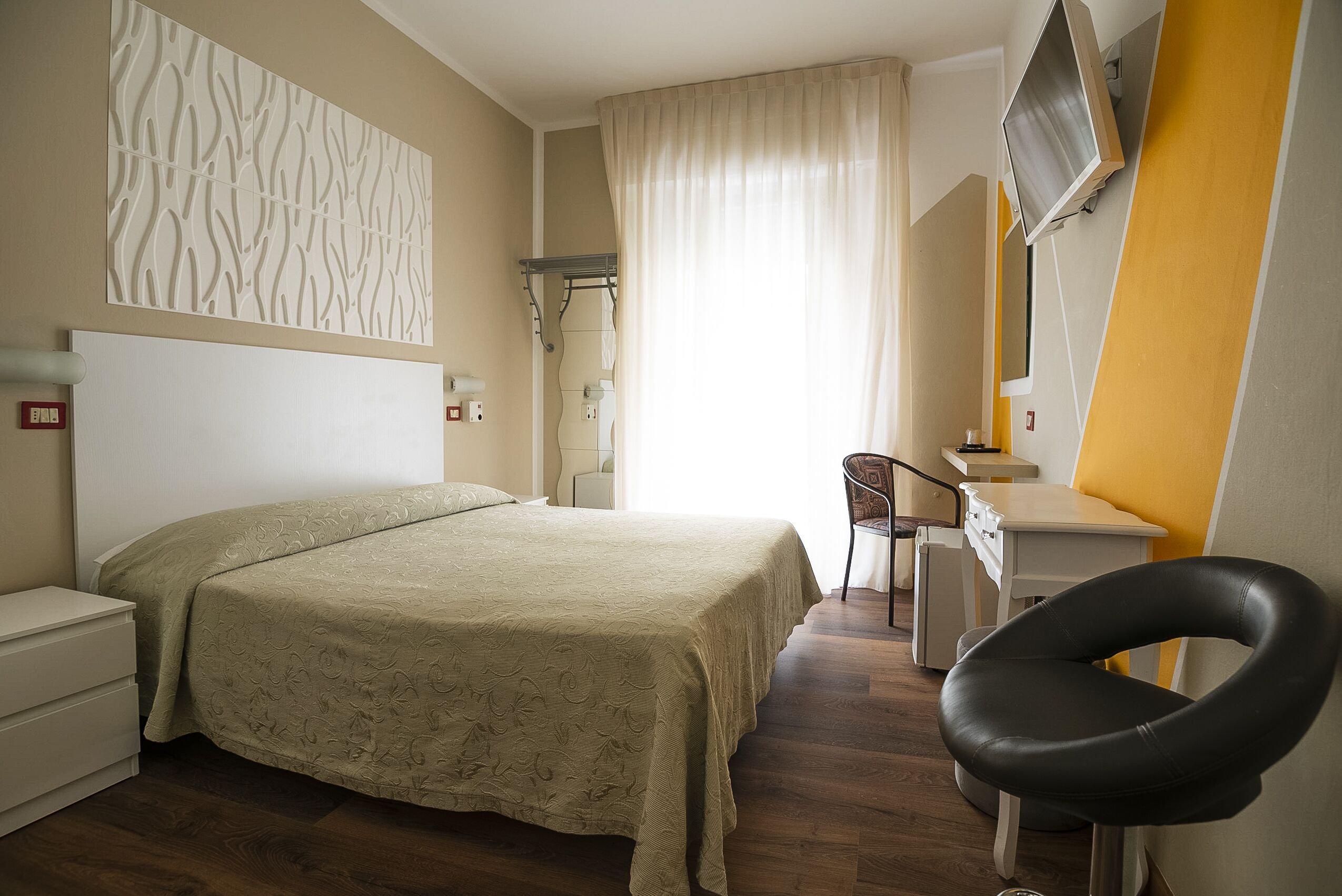 Habitación de hotel con cama, escritorio, silla, televisor y estante en la pared.