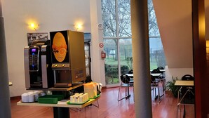 A modern kitchen area with a coffee machine, a display of orange juice, and a view of the outdoors through large windows. - Good Night Hôtel (Arques)