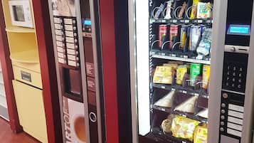 Máquina expendedora con aperitivos y bebidas, un microondas y un refrigerador con un letrero que dice 'POULES POUSSEZ'.
