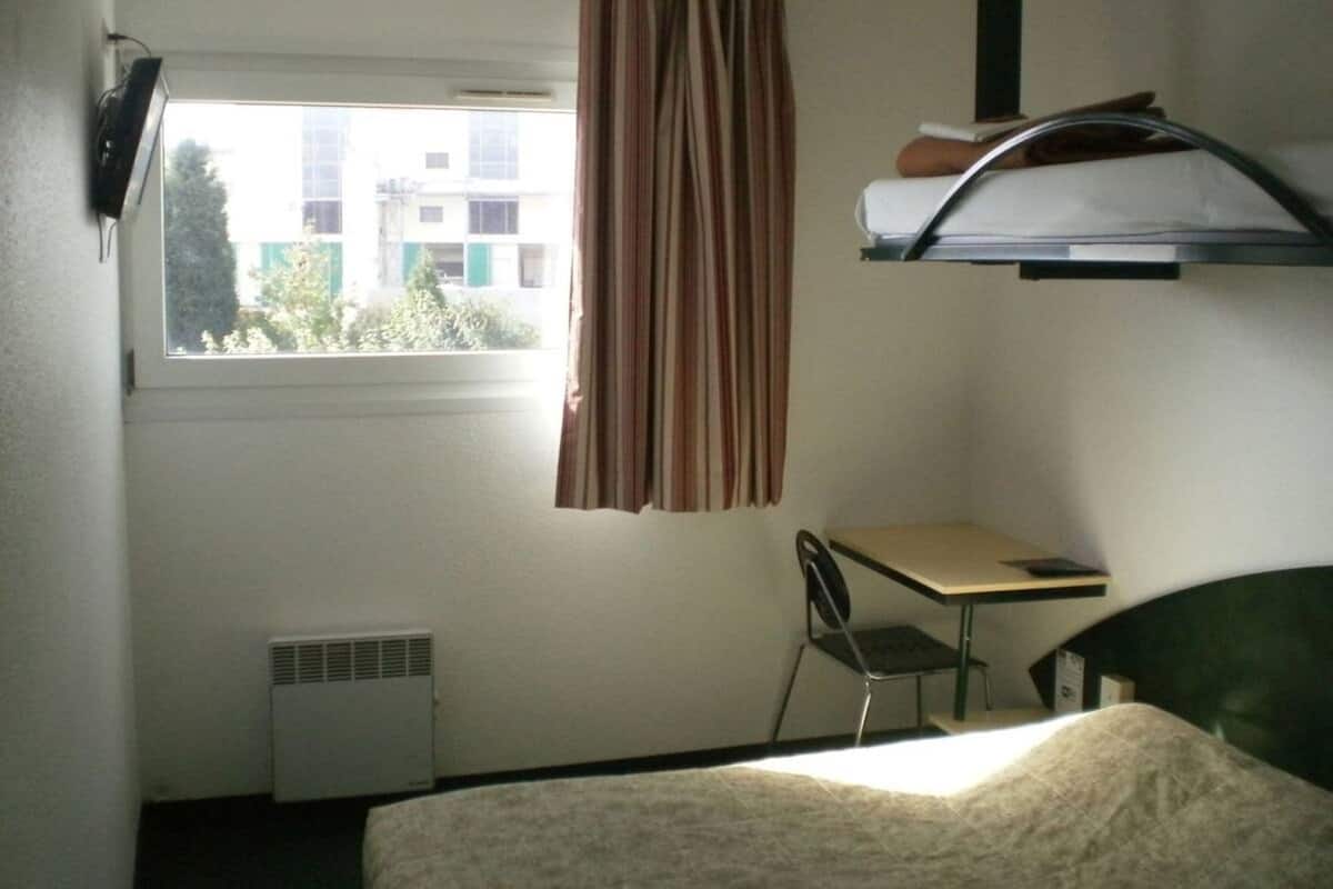 A room with a bed, a desk, a chair, a window with curtains, and a radiator.