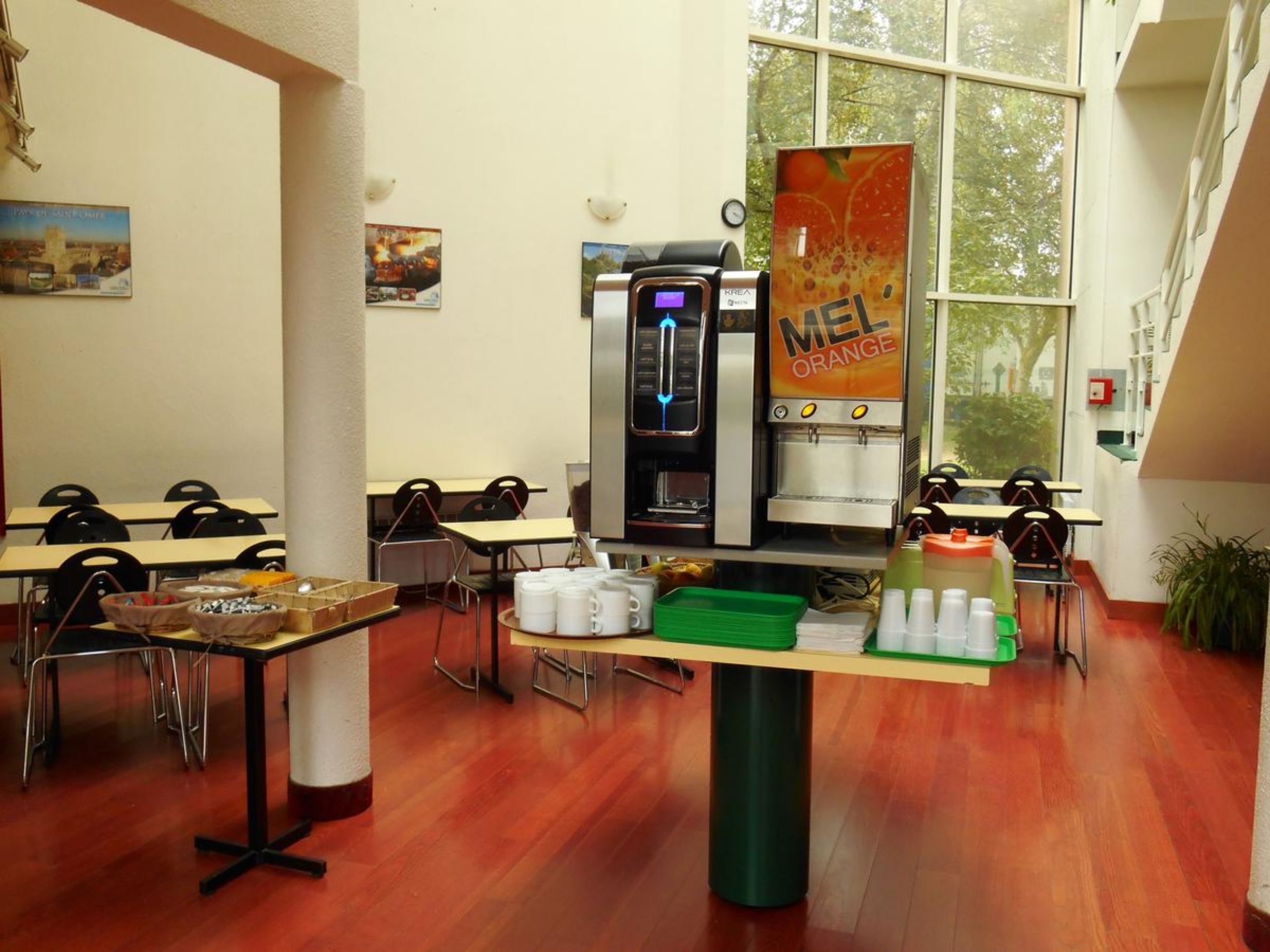 A café with tables, chairs, a coffee machine, and a poster advertising orange juice.