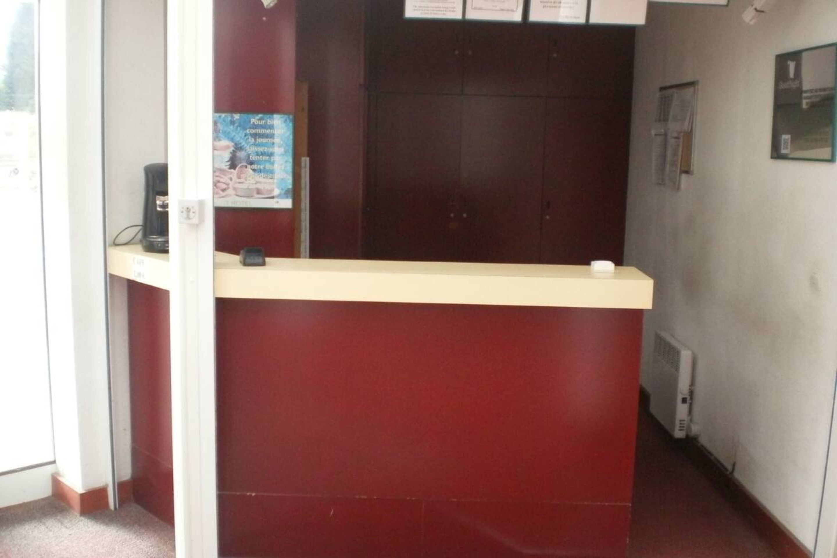 Un comptoir d’accueil avec un plan de travail rouge et un petit appareil noir posé dessus.