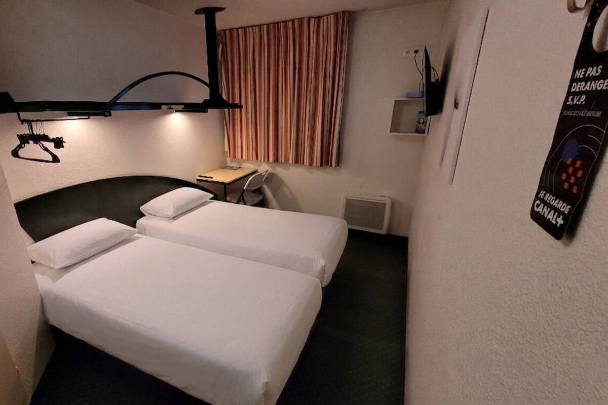 A hotel room with two beds, a desk, a chair, a television, and a poster on the wall.
