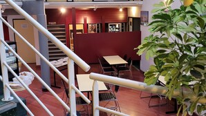 A multi-level indoor space with a staircase, tables, chairs, and a plant. - Good Night Hôtel (Arques)