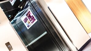A modern elevator interior with a metallic finish and a visible advertisement poster. - Royal Park Boutique Hotel (Budapest)