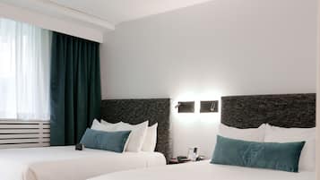 Habitación de hotel con dos camas, un ventanal con cortinas y una lámpara fijada a la pared.