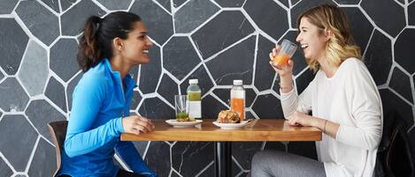 Two people seated at a table with a drink and food, against a black and white patterned wall.