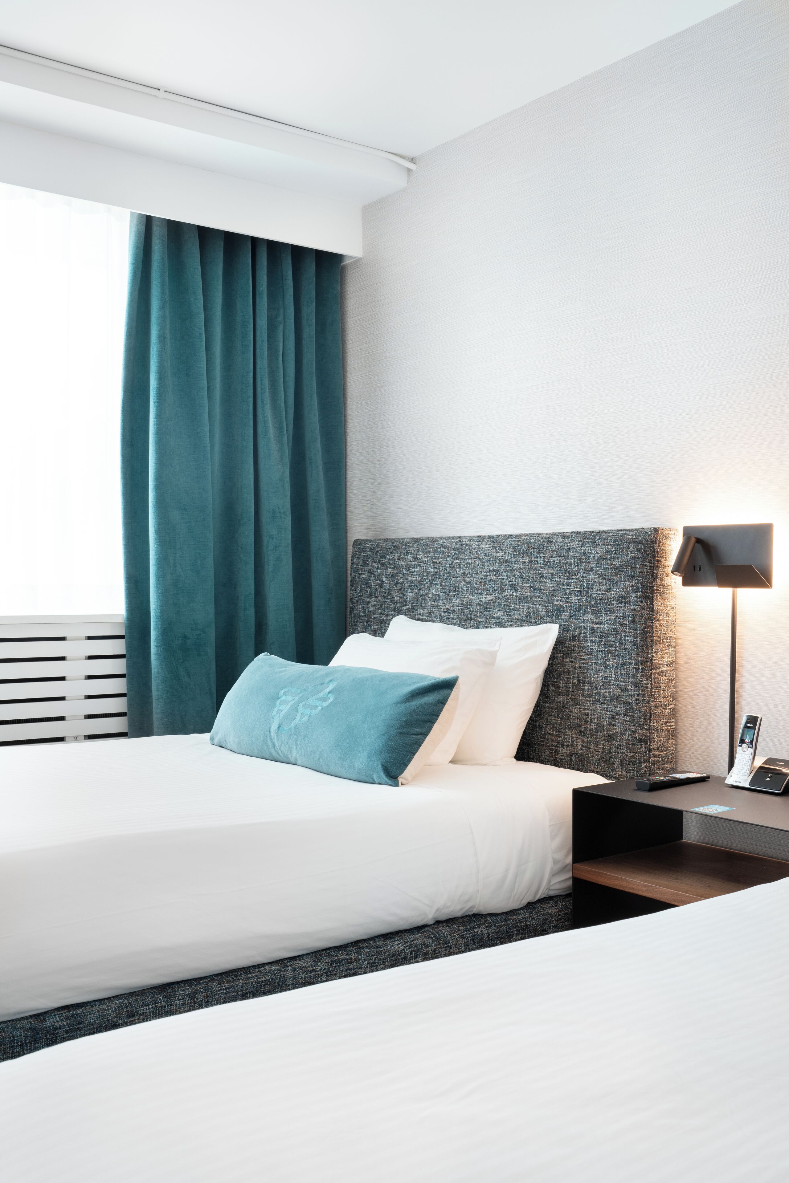 A modern hotel room with a large bed, a nightstand, a lamp, and a window with curtains.