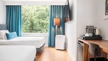 Habitación de hotel con dos camas, un escritorio con cafetera, televisión y vista a los árboles por la ventana.