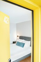 Quarto de hotel com uma cama, mesa de cabeceira e abajur. O número "421" está na parede.