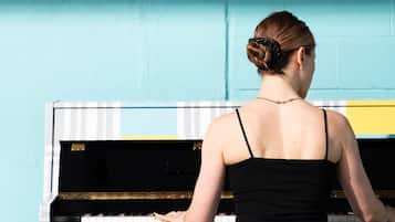 A person playing a piano with a wall text that reads "PLAY YOUR HEART OUT (NOT TOO LOUD NOT TOO LATE)".