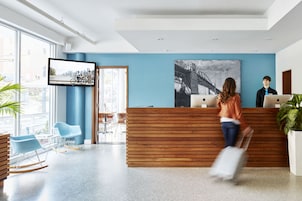 Un área de recepción moderna con un mostrador de madera, un televisor montado en la pared y una gran pintura en blanco y negro de un paisaje urbano.