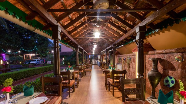 An outdoor restaurant with wooden tables and chairs, a covered roof, and a view of the street. - Casa Severina (Calangute)