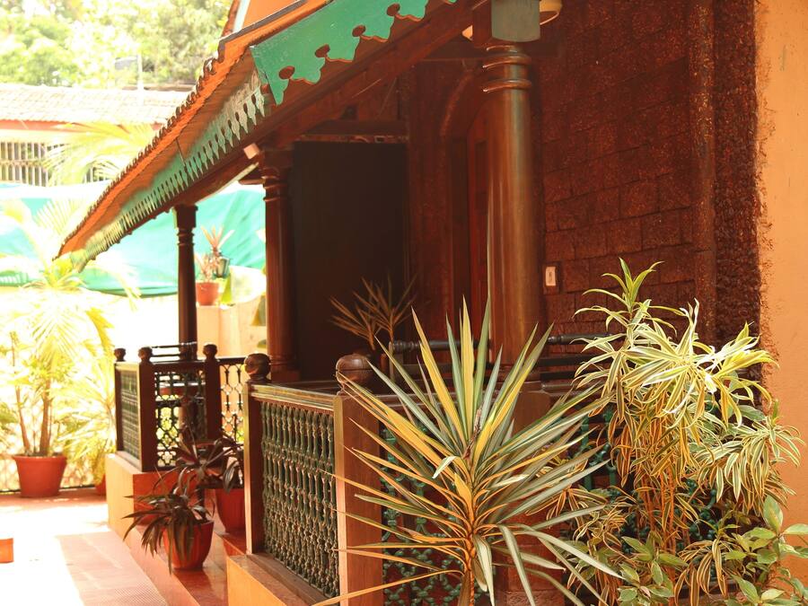 A building with a tiled roof, a porch with a railing, and several potted plants.
