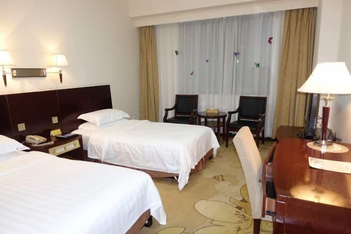 A hotel room with two beds, a desk, a chair, a telephone, and a window with curtains.