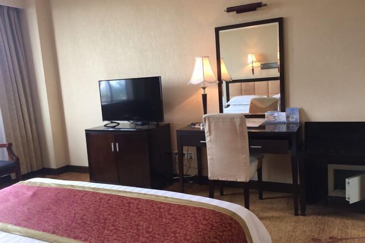 Ein Hotelzimmer mit einem Bett, einem Schreibtisch mit Computer, einem Fernseher und einem Spiegel.