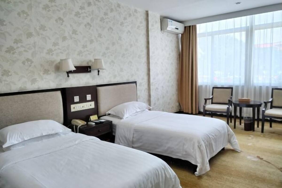 A hotel room with two beds, a desk, a chair, and a small table.