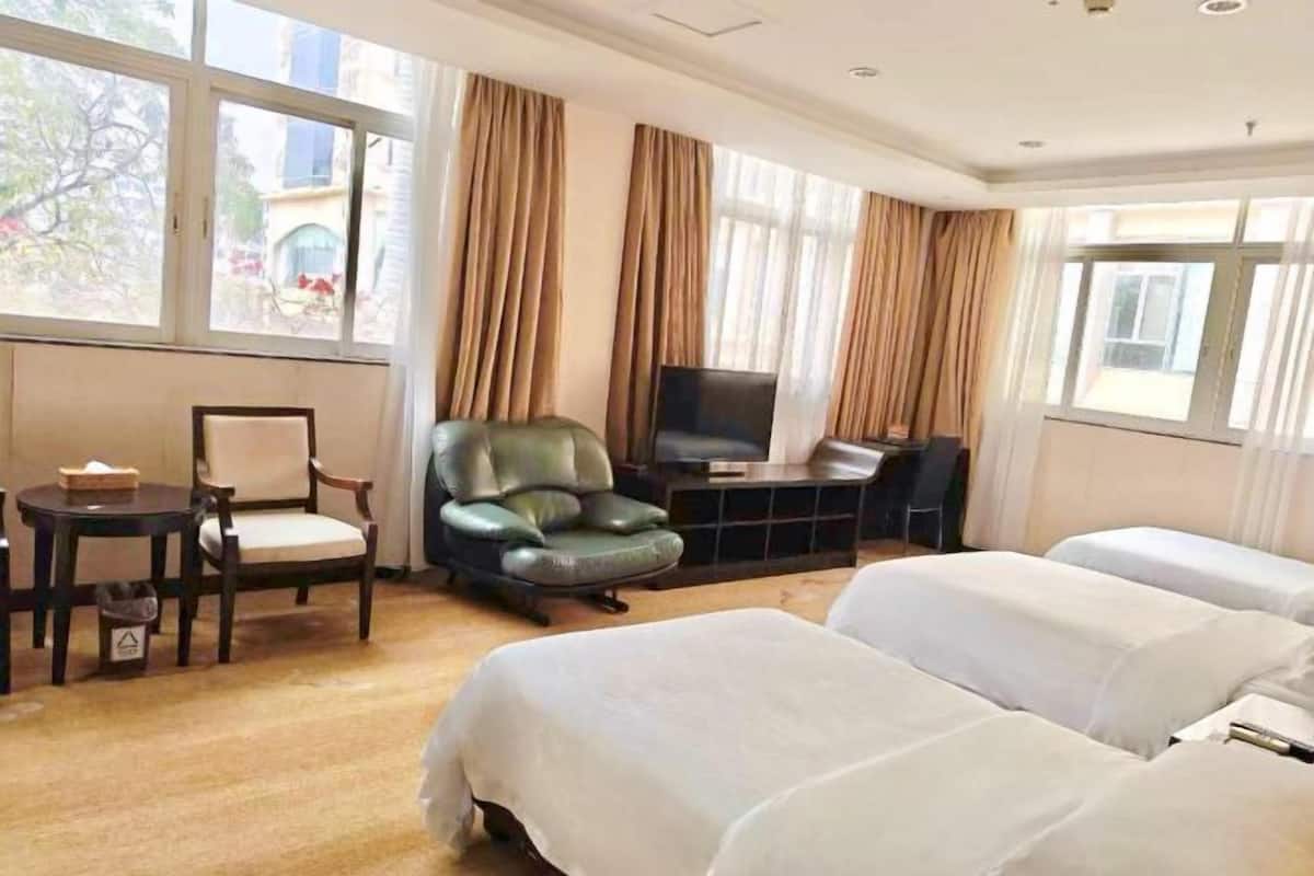A hotel room with two beds, a television, a desk, a chair, and large windows.