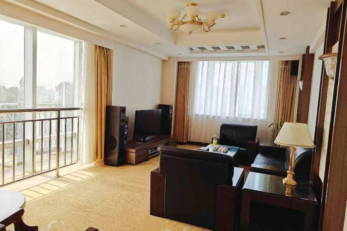 A hotel room with a balcony, a television, a sofa, a coffee table, and a lamp.