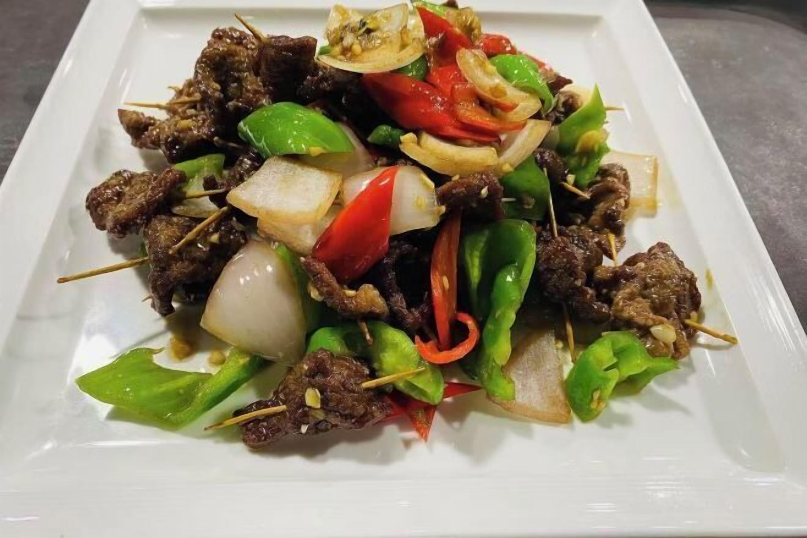 A dish of skewered meat with vegetables on a white plate.