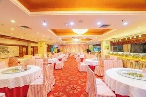 Un salón de banquetes con mesas redondas, manteles blancos y piso cubierto de alfombra roja.